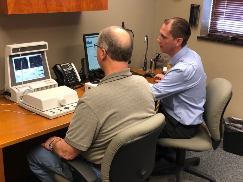 Patient and hearing specialist from Associated Audiologists seated and reviewing test results on specialized equipment.