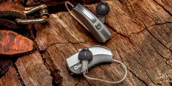 Widex brand hearing aids on a dark-grain wooden surface.