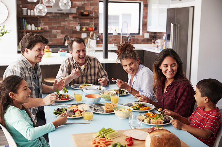 Multi Generation Family Enjoying Meal Around Table At Home Together Family enjoys meal around the dinner table.