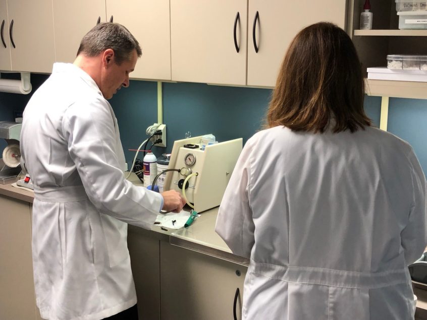 Two hearing specialists at Associated Audiologists working with specialized equipment in a lab.