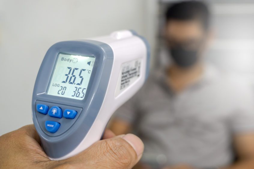 Hand holding infrared thermometer to measure temperature on people with face mask on background