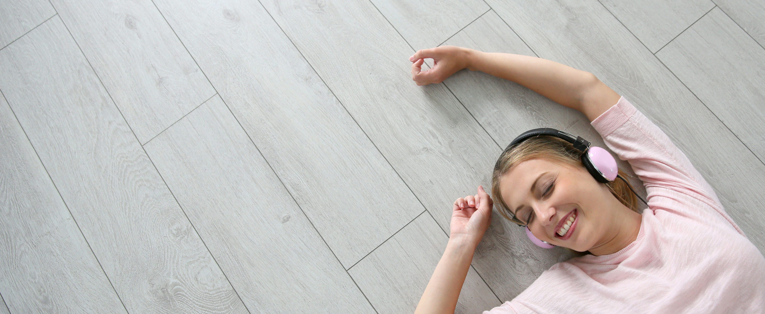 Blond girl relaxing on wooden flooring with headphones on