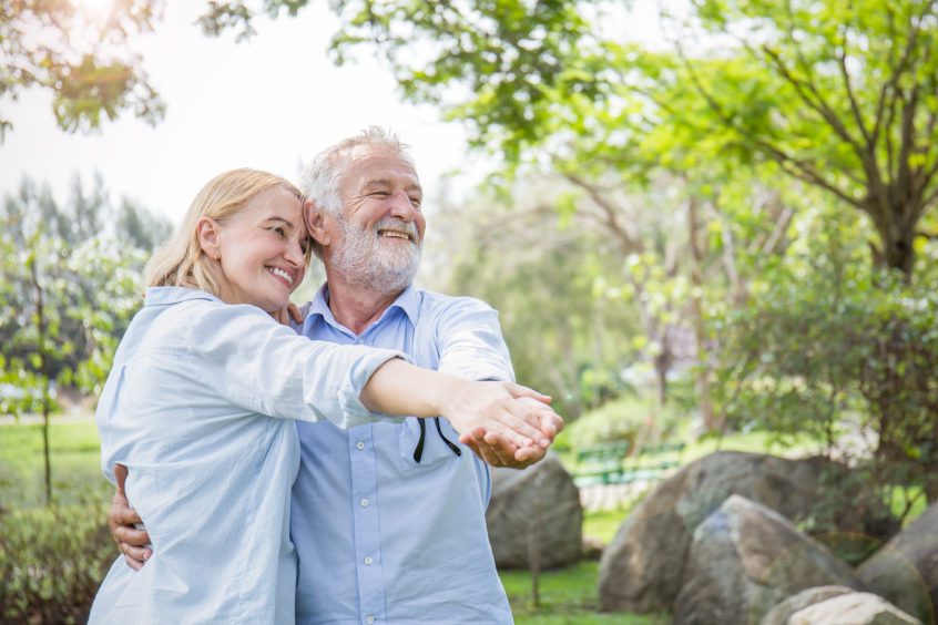 Happy old couple smiling dancing in a park on a sunny day