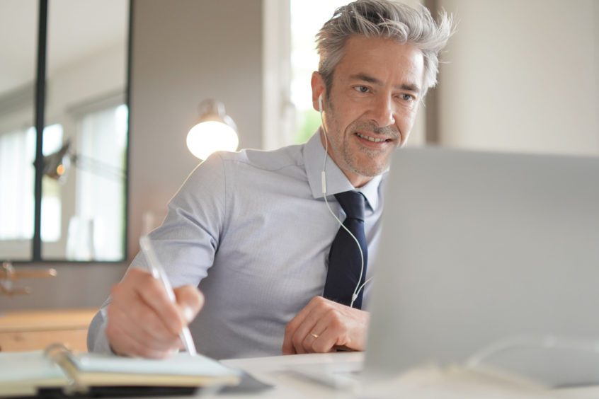 Businessman on video call taking notes in contemporary office