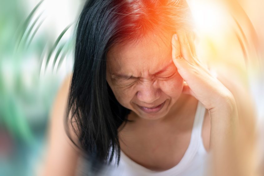 Woman grimacing with hands on her head feeling headache & dizziness