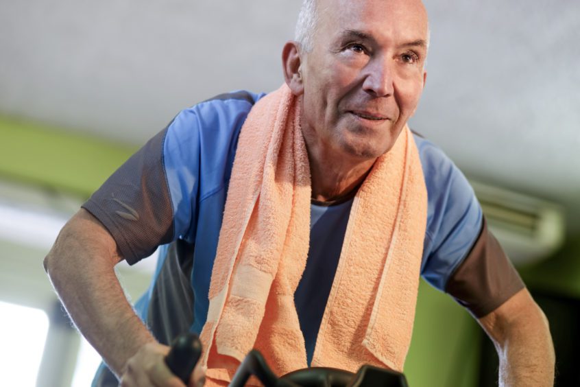 man with orange towel around his neck on stationary bicycle