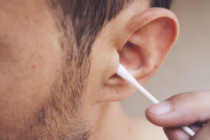 Man about to clean his ears using Q-tip cotton swab to remove wax from ear