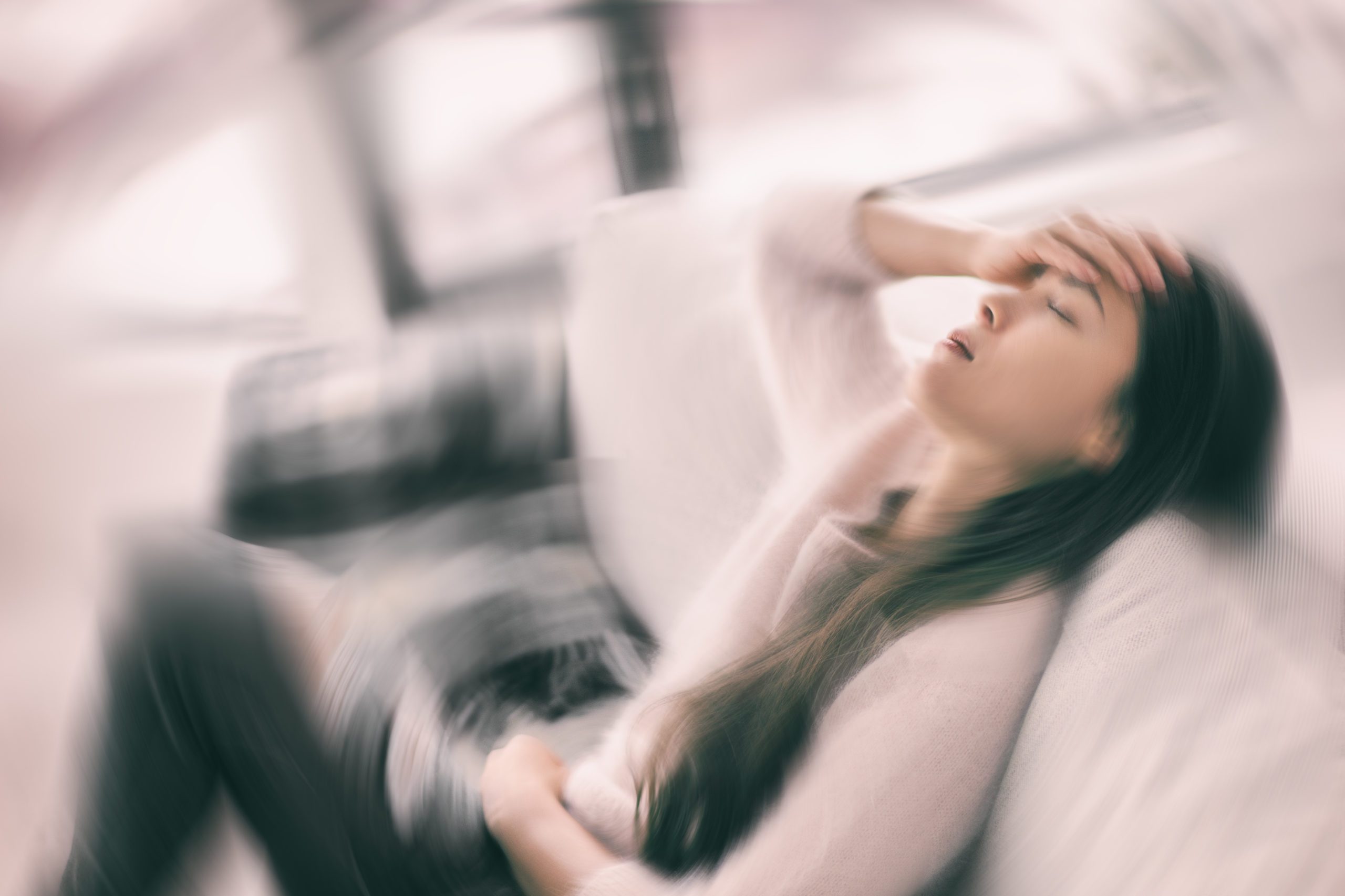 Woman holding her forehead, with radial blur effects to imply vertigo.