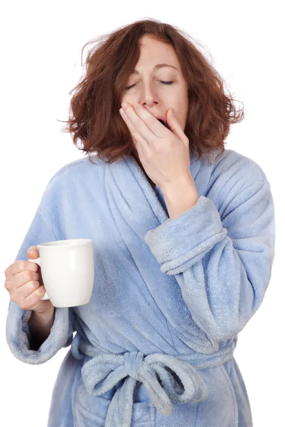 Woman yawning in bathrobe while holding coffee.