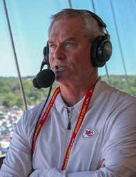 Portrait of Mitch Holthus, wearing a sport broadcast headset and KC Chiefs clothing.