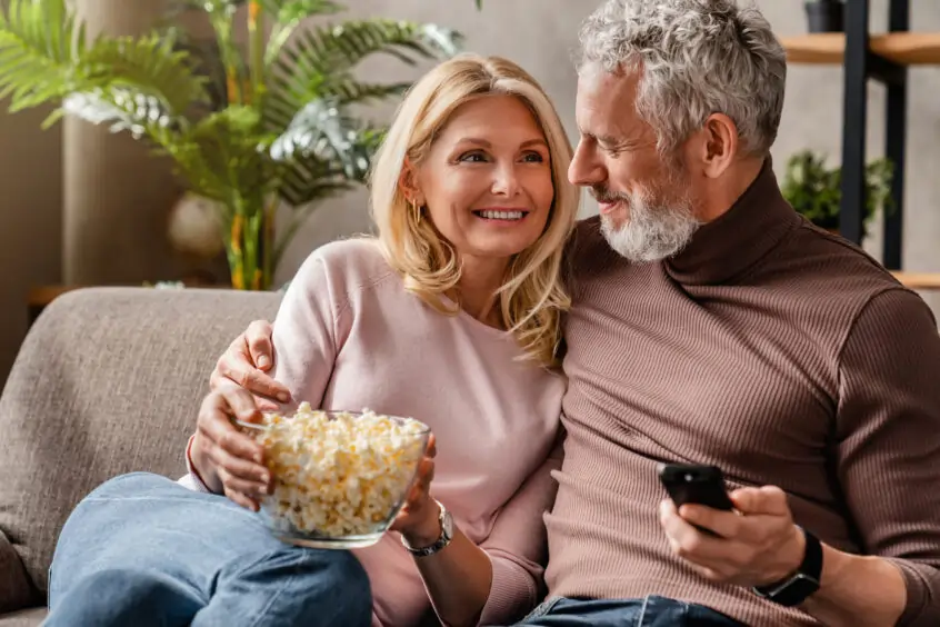 A couple watching tv and enjoying a bowl of popcorn in their living room.