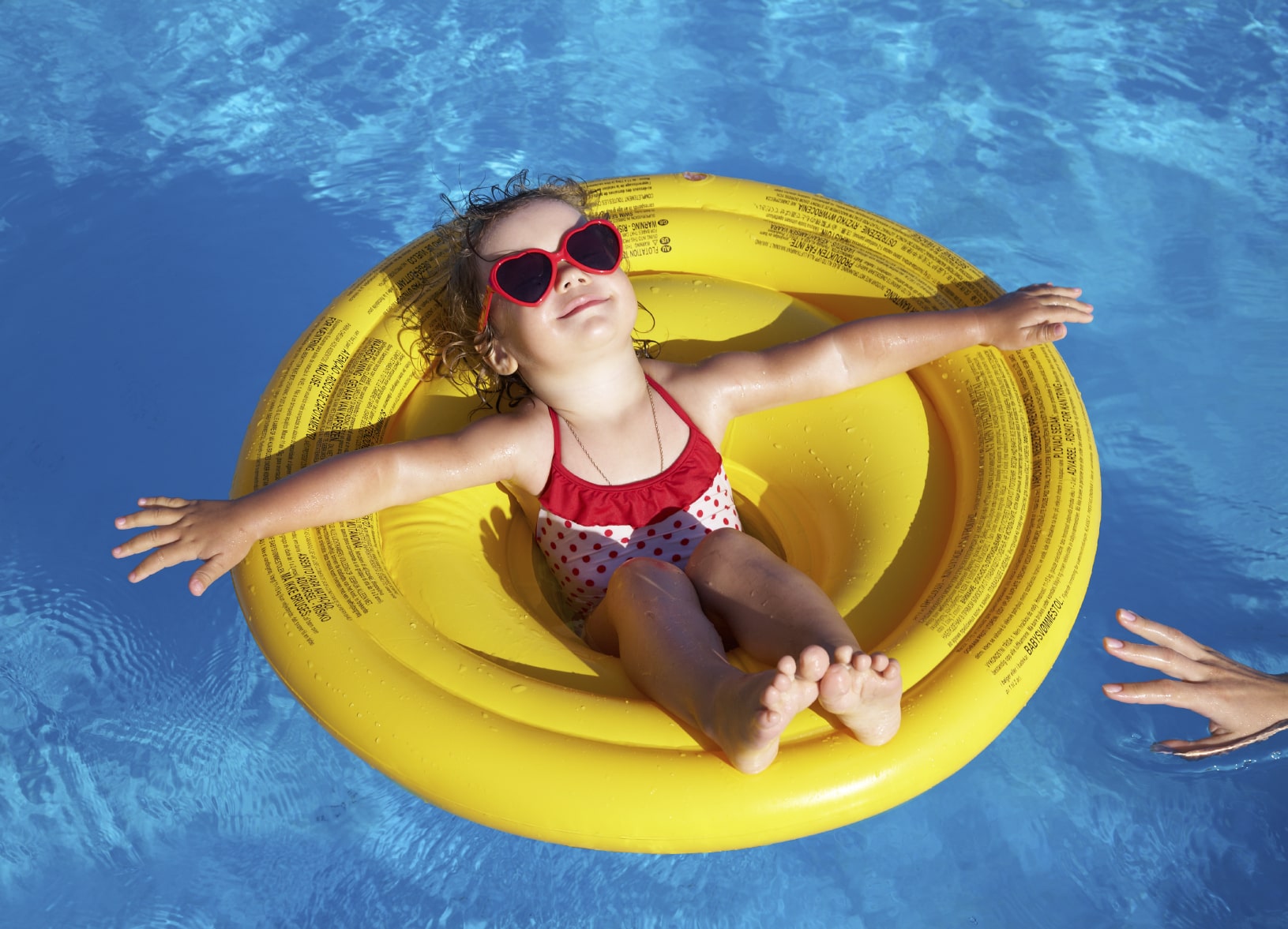 Girl in a yellow inner tube floating in a pool, wearing heart-shaped sunglasses.