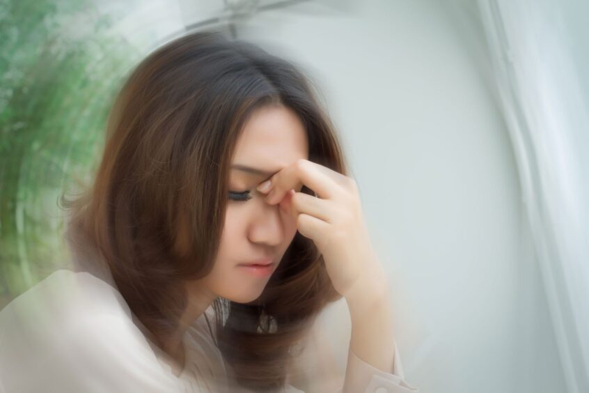 Woman pinching the bridge of her nose with one hand, with an exaggerated radial blur effect in the background.