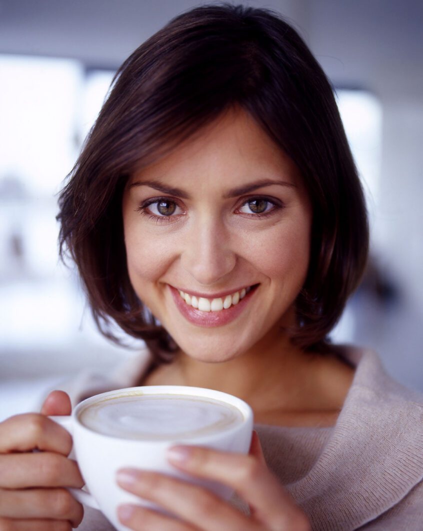 Woman posing for a photo while holding a cup of coffee with both hands.