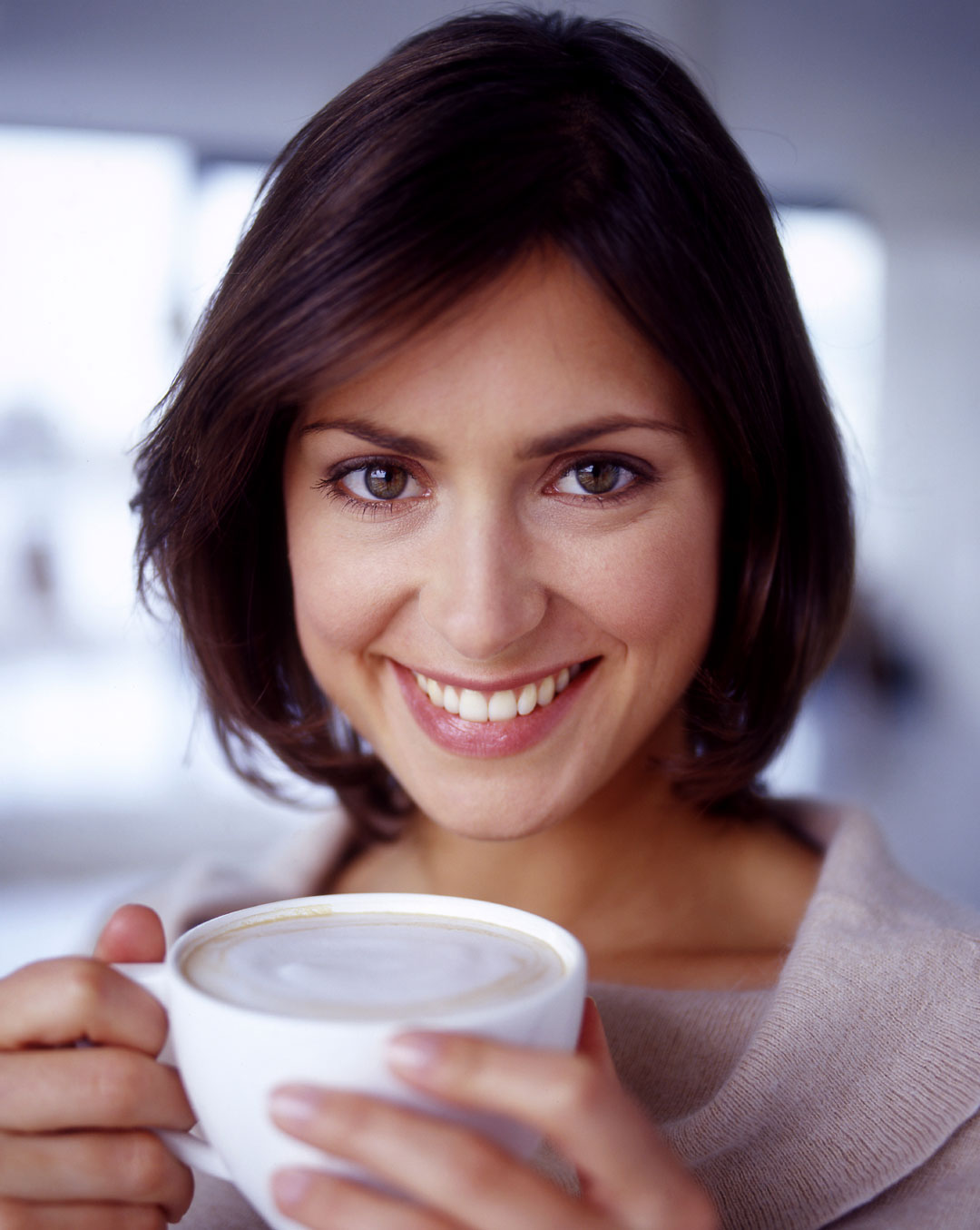 Woman posing for a photo while holding a cup of coffee with both hands.