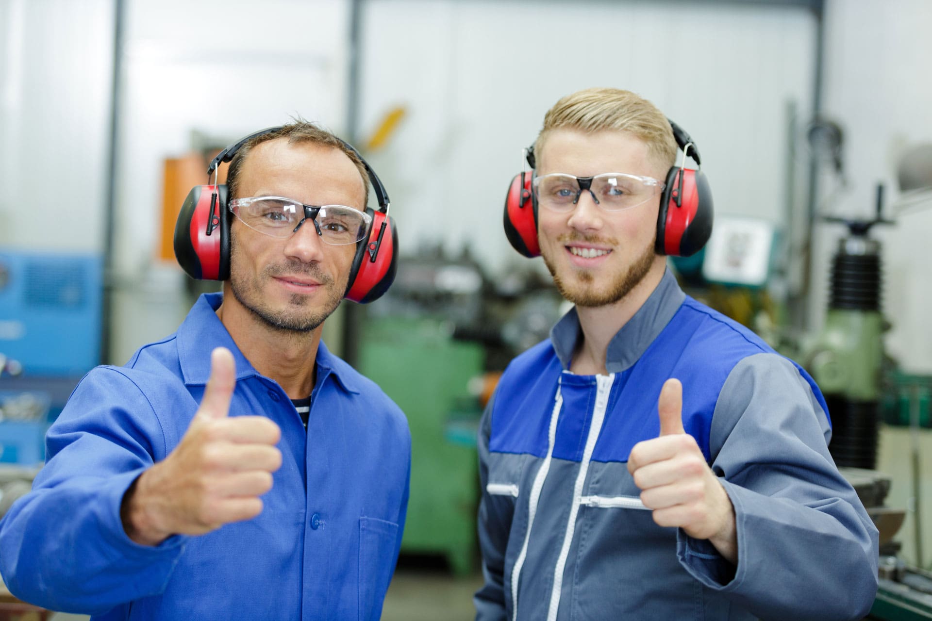 Two manufacturing workers giving a thumbs-up while wearing hearing protection earmuffs.