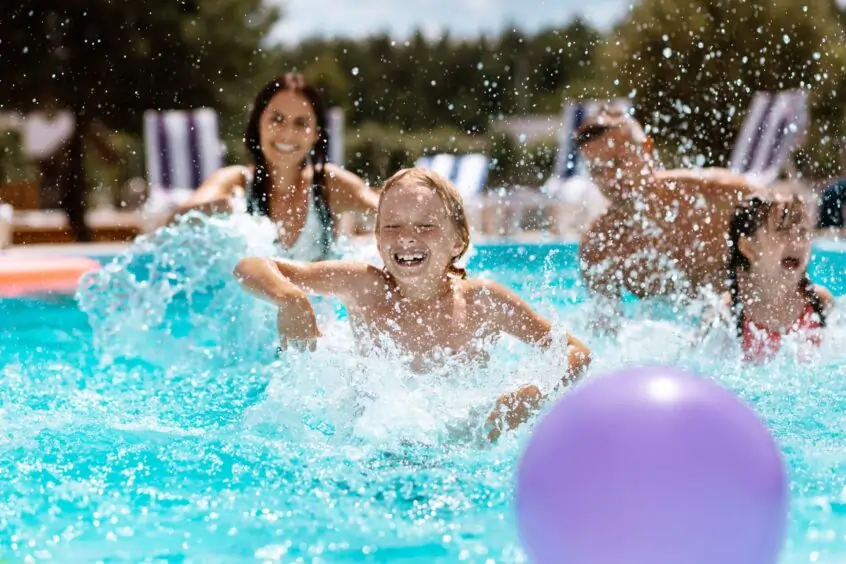 A family captured mid-action while playing in a waist deep pool. A purple ball is in the foreground.